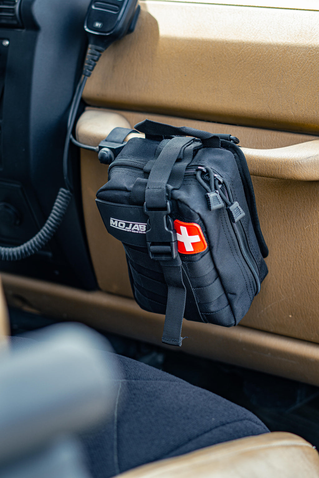 Red, Black, Orange and Green First Aid Kit with a Swiss flag patch on a Jeep grab handle.