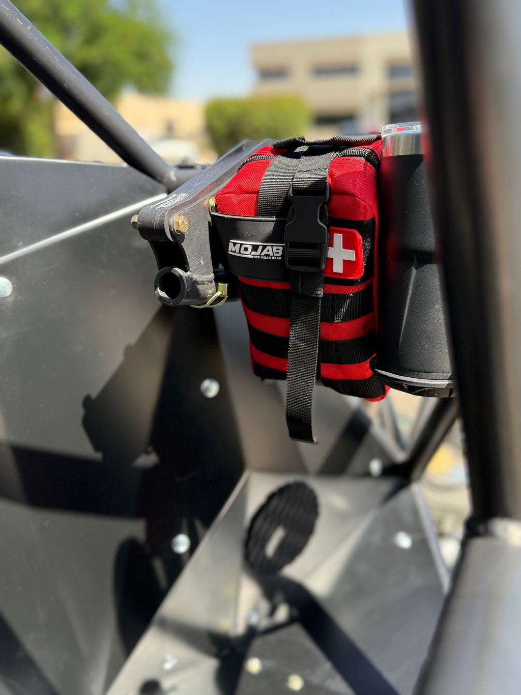 Red, Black, Orange and Green First Aid Kit with a cross symbol on a vehicle roll cage.